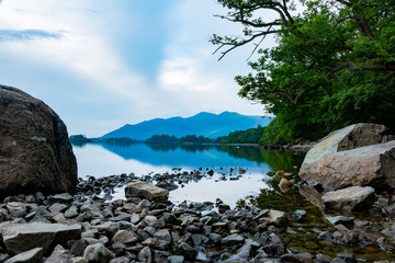 Fototapeta na wymiar Stones in the lake with a fragment of a pebble beach with mountains nicely reflected in the water - Keswick, Lake District, United Kingdom