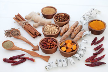 Spices for slimming and weight loss with fresh and dried turmeric, cumin, ginger, chilli, cinnamon and gymnema sylvestre used to suppress appetite. Top view on white wood background.