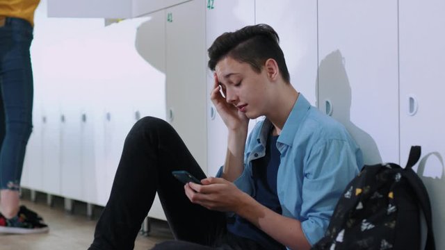 Profile of upset college student sitting by lockers in the school corridor. handsome young boy in trouble using a smartphone trying to get things done.
