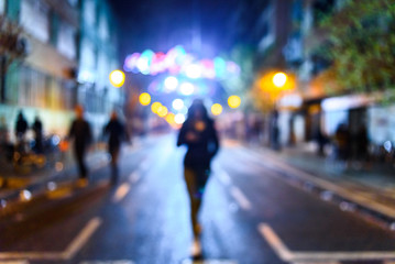 Urban night scene with people walking out of focus with colored background.