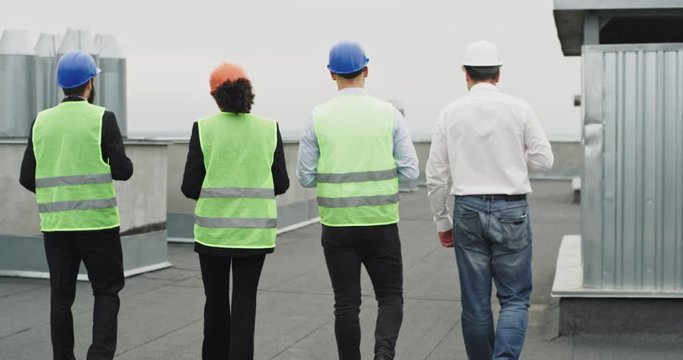 Architect and two engineers walking through the construction site on the rooftop and analyzing the plan they wearing the safety helmets