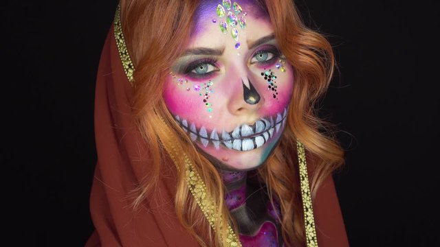 charming lady in image of dead beauty, spiritual beauty and brilliant make-up of sugar skull on face, deceased princess with rhinestones on pink makeup, girl with red hair and gold plated head