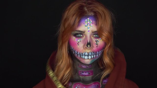charming girl with sugar skull, image of joyful death and happy afterlife, priestess prepares for rite with dead souls and removes hood with red fiery hair, fairy tale about magic and secrets