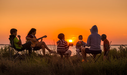 people sitting on the beach with campfire at sunset