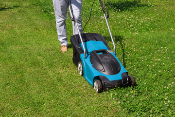 Obraz premium Woman gardener with an electric lawn mower on a grass lawn with half mowed grass with copyspace