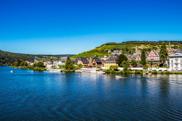 Fototapeta na wymiar View to Middle Moselle River with cruise ships and Traben -part of the beautiful town of Traben-Trarbach with steeply sloped vineyards in the background, cloudless sky, Germany