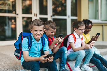 Group of happy elementary school students with smartphones. Primary education, friendship, childhood, and technology concept.