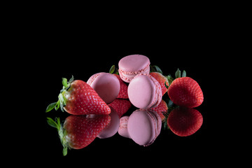 Strawberries and delicious macaroons stacked on a glass table with a black background