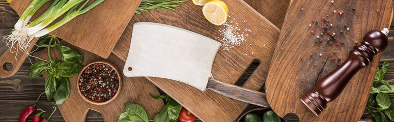 panoramic shot of cutting boards, cherry tomatoes, salt, chili peppers, pepper mill, meat chopper, lemon, greenery and spices