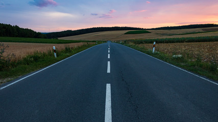 Empty straight asphalt road against sunset sky in rural landscape.