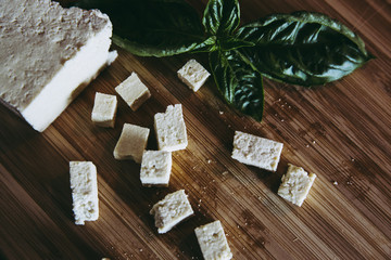 Cuts of fresh tofu small pieces with green basil on wooden kitchen board. home vegan food