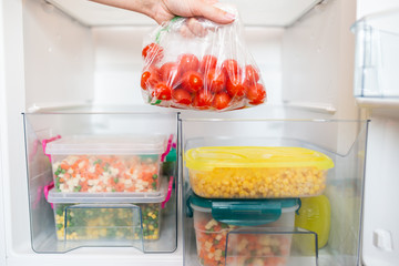 Woman putting bag with cherry tomatoes in refrigerator.