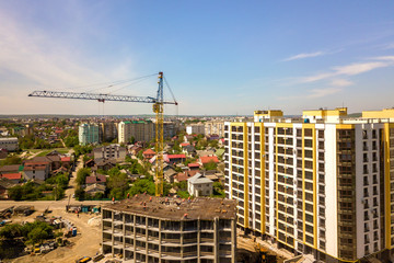 Apartment or office tall building under construction. Working builders and tower cranes on bright...