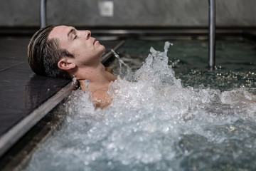 Attractive male lying in bubbling jacuzzi - obrazy, fototapety, plakaty