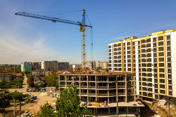 Apartment or office tall building under construction. Working builders and tower cranes on bright blue sky copy space background.