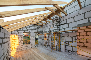 House interior under construction and renovation. Energy saving walls of hollow foam insulation blocks and bricks, ceiling beams and roof frame.