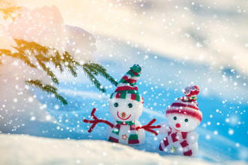 Two small funny toys baby snowman in knitted hats and scarves in deep snow outdoors on bright blue and white copy space background. Happy New Year and Merry Christmas greeting card.