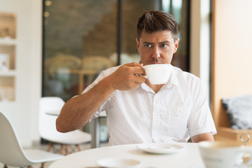 A man drinking coffee from a white cup in a cafe