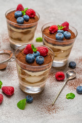 Classic tiramisu dessert with blueberries and raspberries in a glass and strainer with cocoa powder on concrete background