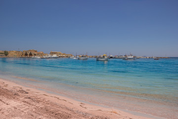 Fototapeta na wymiar Marzamemi Sicily, beautiful beach and clear sea, with the historical village in background
