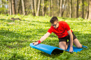 Man spreads a blue yoga mat in a park on green grass for exercises and relaxation. Healthy lifestyle