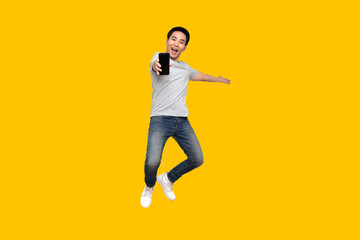 Fototapeta na wymiar Asian man jumping and presenting mobile phone isolated on yellow background