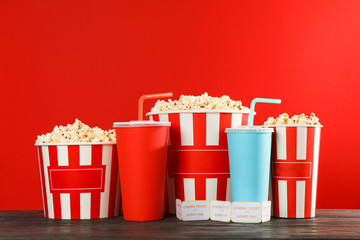 Popcorn buckets, paper cups and tickets against red background, space for text