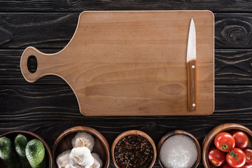 top view of cutting board, cherry tomatoes, salt, garlics, cucumbers, knife and spices