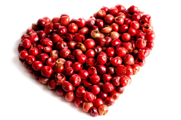 Pink peppercorns in a heart shape on white textured background. Top view
