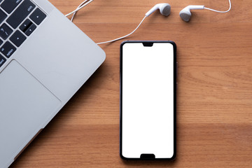 Smartphone screen blank headphones and computer notebook on wood background