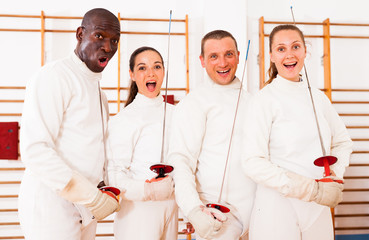 Positive fencers standing with foils  together at fencing workout