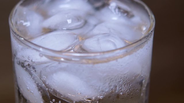 Macro Closeup Glass of cold refreshing fizzy drink with ice cubes. Soda with Ice in glass. Mineral bubbles. 360 rotation. 4K UHD video footage