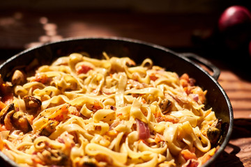 Spaghetti, pasta with mussels, tomatoes, onions and cream sauce in a pan.