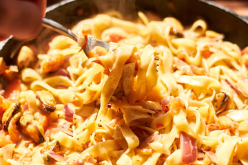 Spaghetti, pasta with mussels, tomatoes, onions and cream sauce in a pan.