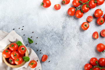 Bunch of juicy organic red cherry tomatoes arranged w/ green basil leaves in wooden laptop, stone...