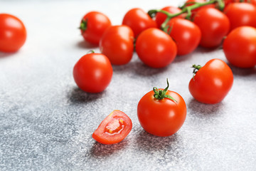 Branch of juicy organic red cherry tomatoes arranged in row and scattered on grunged stone background. Polished vegetables. Clean eating concept. Vegetarian diet. Copy space, flat lay, top view.