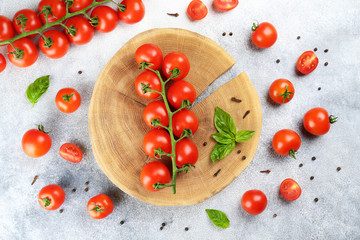 Bunch of juicy organic red cherry tomatoes arranged w/ green basil leaves on wooden slice, stone background. Polished vegetables. Clean eating concept. Vegetarian diet. Copy space, flat lay, top view.