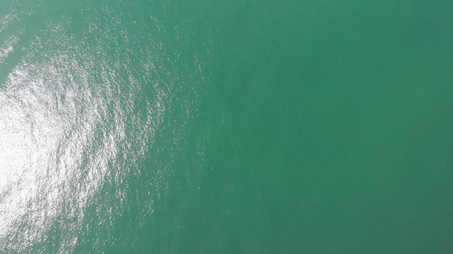 An aerial backward footage of a rocky island rock (Thatcher Point) along rocky cliff and turquoise water under a majestic blue sky