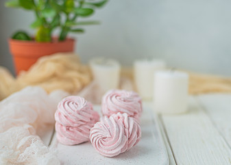 Obraz na płótnie Canvas homemade Marshmallow zephyr on a white plate with candles and room tree on a light wooden table. Pink sweet homemade marshmallow. Colorful meringues on a white background. dessert