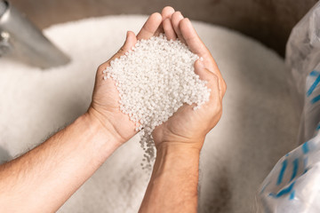 View of modern factory worker hands holding pile of white polymer pellets - obrazy, fototapety, plakaty