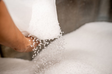 Small plastic granules scattering out of white sack held by worker
