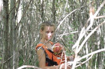 A young mother with a child in a sling in the forest