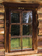 Window in an old rustic log house with the reflection of meadow