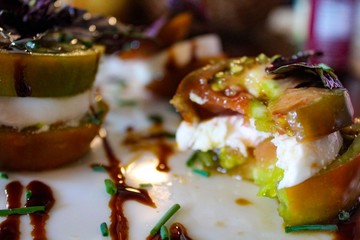 Selective Focus of Organic Caprese Salad Stacks with Heirloom tomatoes, fresh mozzarella and purple basil drizzled with balsamic reduction on white platter