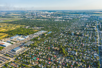Aerial view from drone. Aerial view of the suburbs with the city, giant smoke stack in industrial area, far villages and fields. Sunny days ahead, sunset real estate suburb homes.