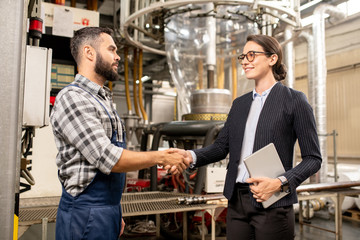 Two young business partners shaking hands after making deal in factory