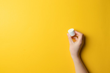 Fototapeta na wymiar Close up shot of hands applying moisturizer. Beauty woman holding a plastic jar with skin cream on a yellow background.