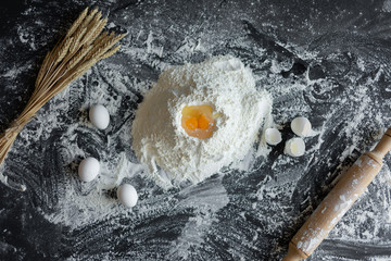 Ingredients for baking - dough, flour, wooden spoon, rolling pin, eggs, egg yolks on a dark...