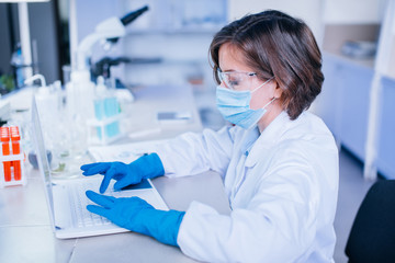 Scientist typing into the computer wearing all the safety wear.