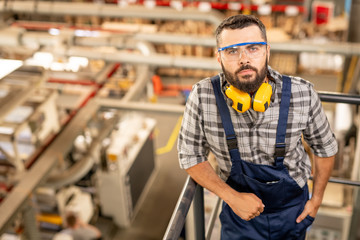 Serious technician of large factory in protective eyeglasses and headphones